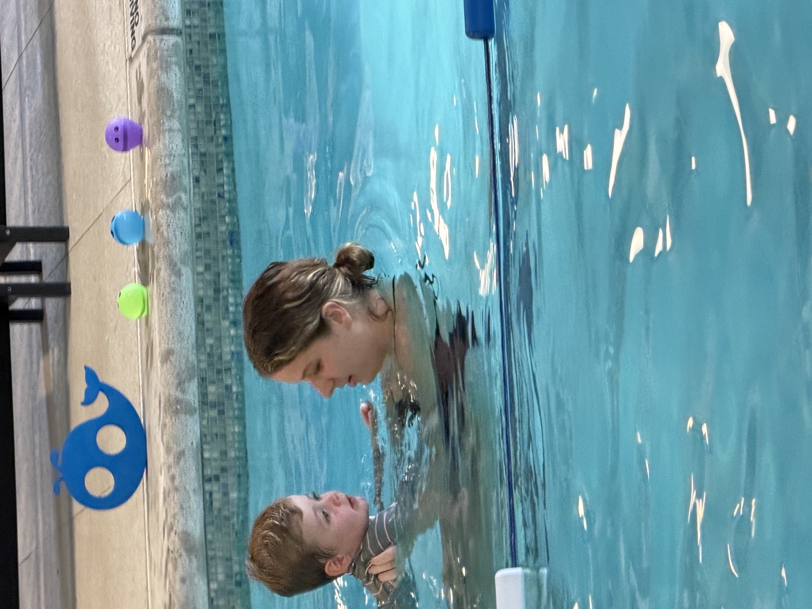 A coach in the water face to face with a young child during a Side by Side parent and child swim lesson