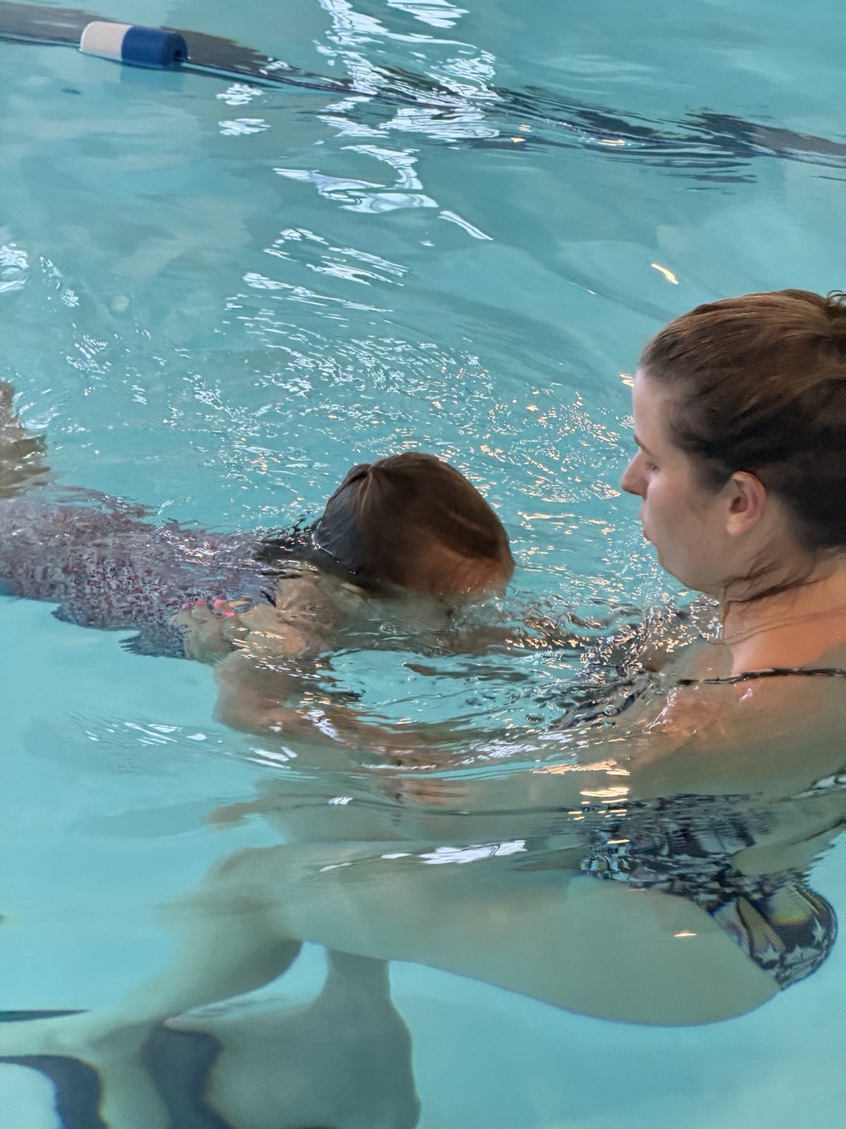 Coach supporting a young swimmer at the surface during a survival skills lesson
